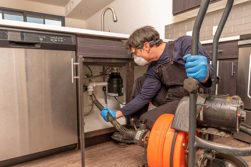 plumber wearing a safety mask, using an auger Norman, OK